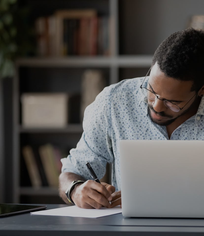 Concentrated African American male worker sit at desk handwrite watching webinar or training on lapt...
