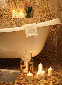 Home bathroom interior with bubble bath, candles, magazine and white whine. Relax concept
