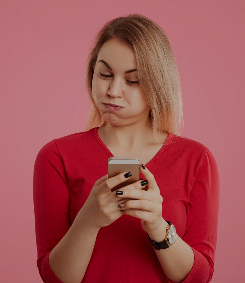 A woman looks frustrated and confused at her phone.
