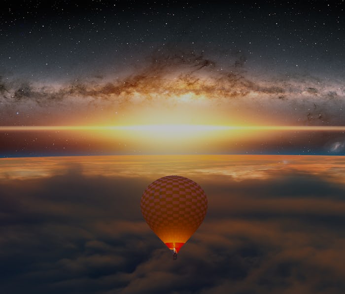 Hot air balloon flying over sunrise clouds with earth planet sunrise milky way galaxy in the backgro...