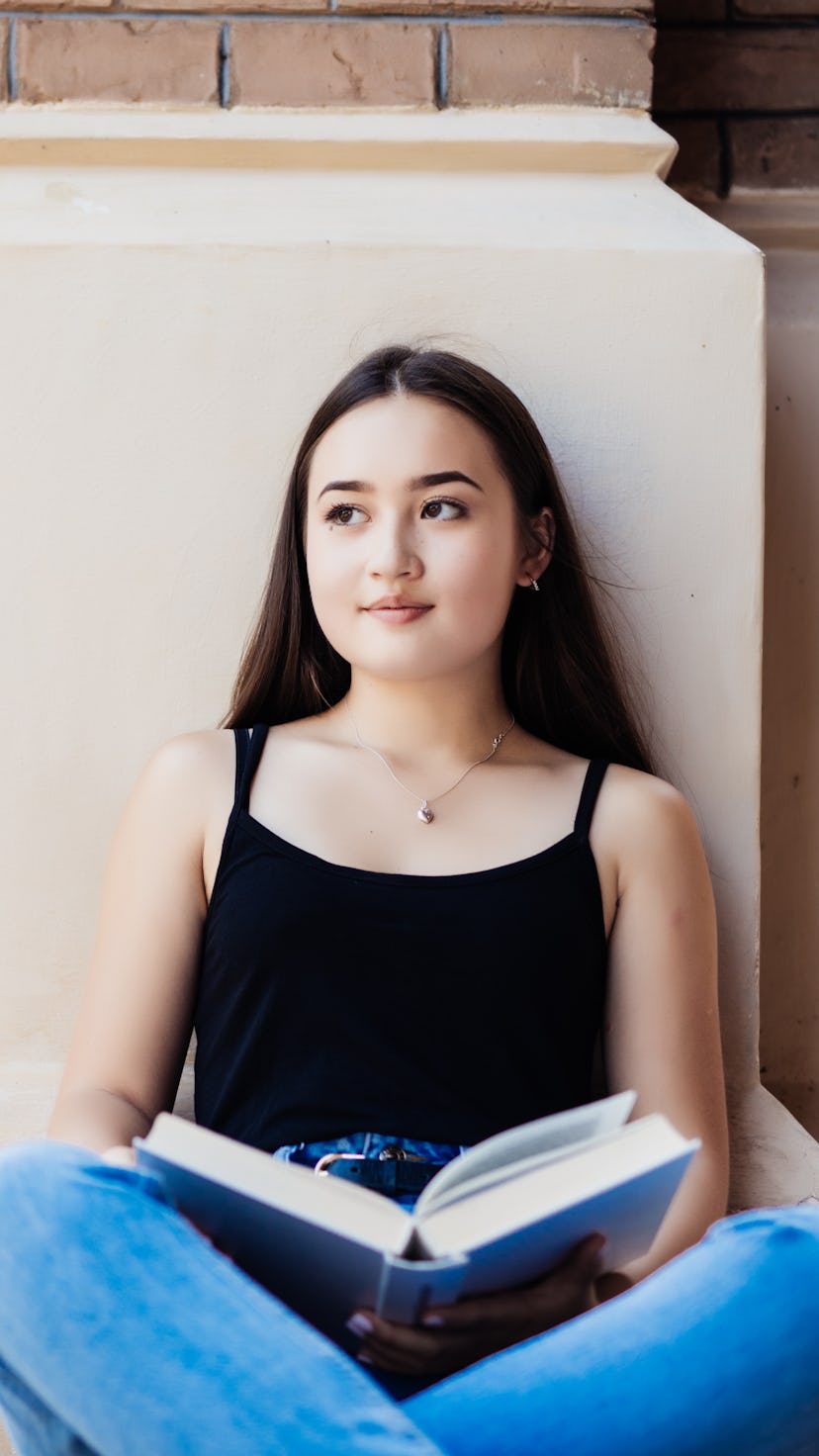 Young woman sits holding a book and smiling