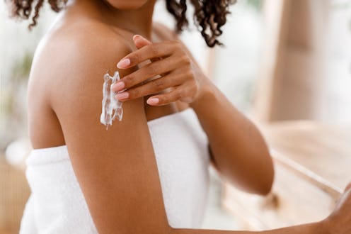 Skin Care Products Concept. Black woman applying moisturizing lotion on body after shower, standing ...