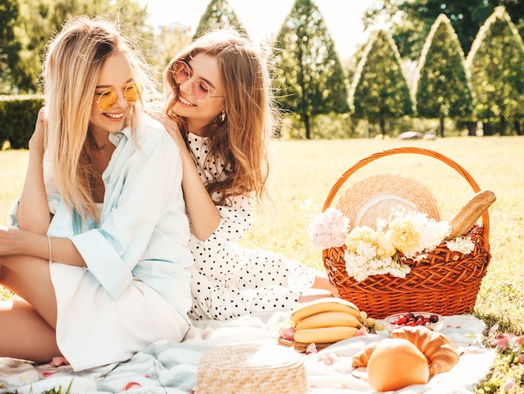 A happy couple enjoys a spring picnic outside with a basket filled with food and gifts.