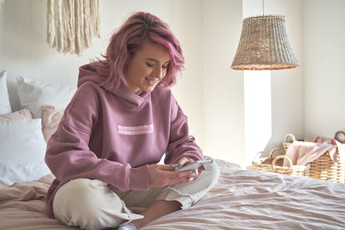A woman sitting in trendy pink room looking at #BamaRush 2022 dorm inspiration on TikTok.