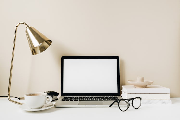 Blank screen laptop. Home office desk table workspace with coffee, lamp, glasses, notebook on beige ...