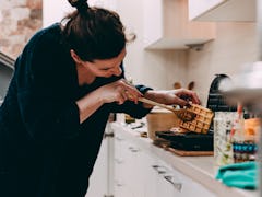A woman checks out the waffle she's making in her kitchen. 