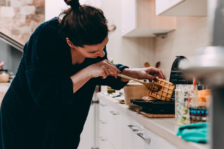 A woman checks out the waffle she's making in her kitchen.
