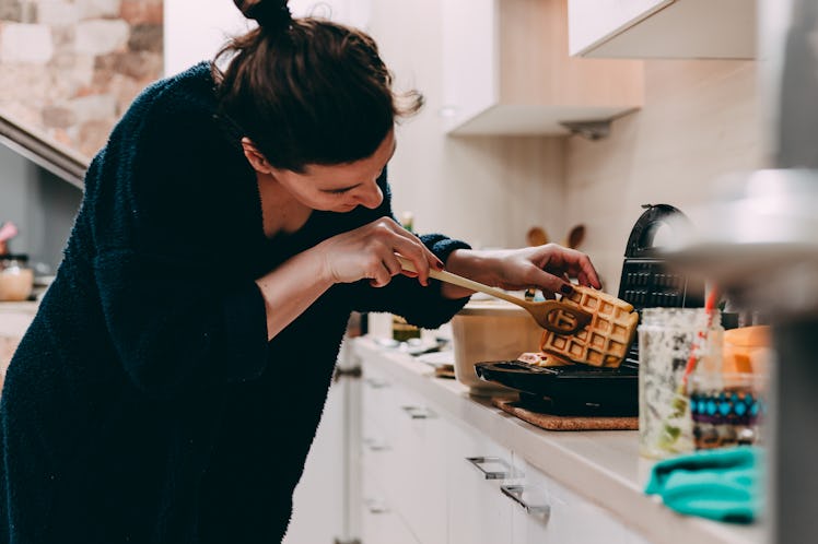 A woman checks out the waffle she's making in her kitchen. 