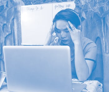 A young Asian teacher is stressed out and massages her temple during a video conference call.