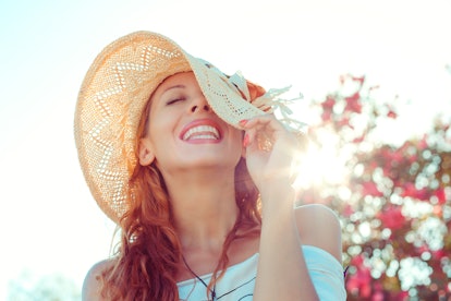 Happy girl. Woman in hat looking up wards smiling happy pulling hat down on face laughing isolated g...
