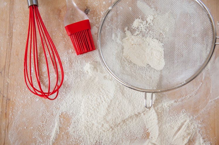 Overhead cooking background. White flour and red silicone tools on wooden cutting board. Baking proc...