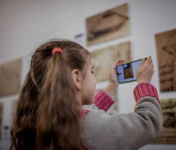 Curious girl exploring a contemporary art exhibition with augmented reality mobile application, futu...