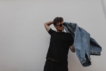 Modern young man hipster puts on a stylish denim jacket. Attractive guy in fashionable clothes in su...