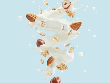 Fresh milk or yogurt splash swirl with cereals, hazelnuts, almonds, cornflakes isolated. Healthy bre...