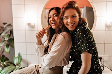 Two friends laugh while hanging out in the bathroom together. 