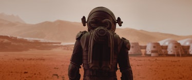 Back view of astronaut wearing space suit walking on a surface of a red planet. Martian base and rov...