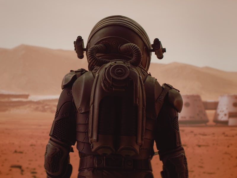 Back view of astronaut wearing space suit walking on a surface of a red planet. Martian base and rov...