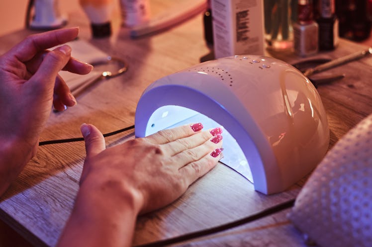 Client with red varnish at manicure salon cairfully waiting when her nails become dry in UV light. ...