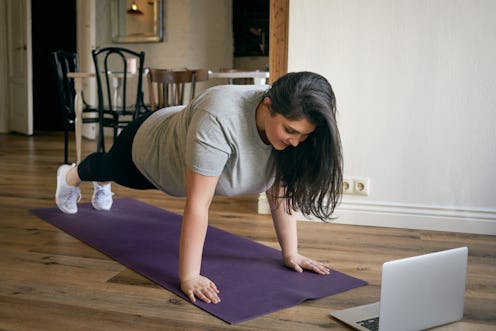 Energetic self determined overweight young woman in sneakers standing in plank with feet and hands o...