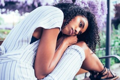 Young sad black woman sitting surrounded by flowers