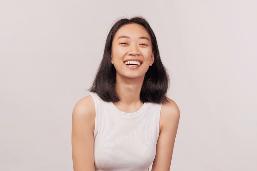 Girl laughs at something funny closes eyes with pleasure. Businesslike young woman Asian appearance ...