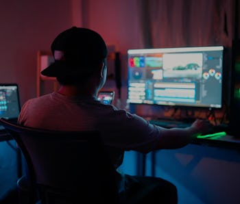 Blogger working editing video footage and looking at the monitor in-home office while working on pos...