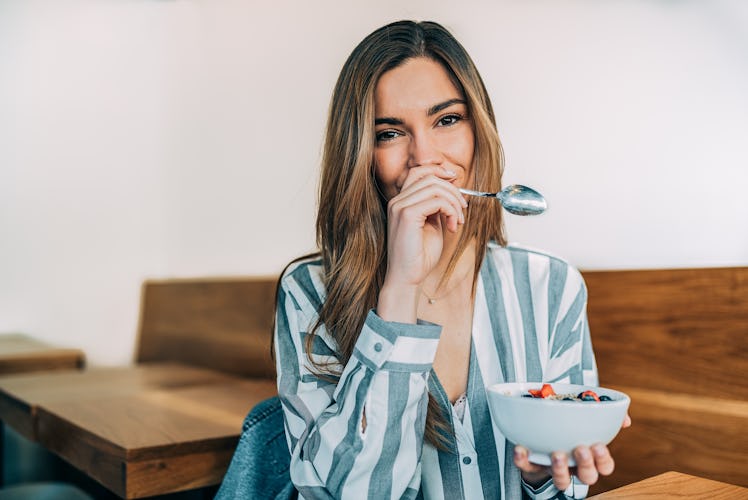 A woman holds a bowl of fruit with a spoon in her other hand.