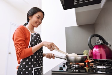 A happy woman cooks something over her stove at home.