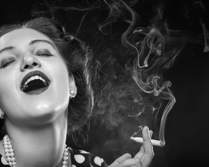 happy young woman smoking joint on black background, monochrome
