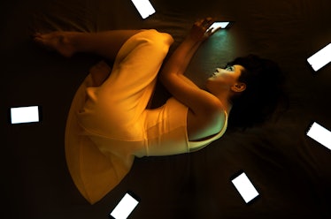 Cute girl in orange dress lying in the dark on her bed surrounding with cellphones conception mean s...