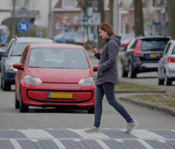 young woman walks on the crosswalk and checks her smartphone for messages and does not pay any atten...