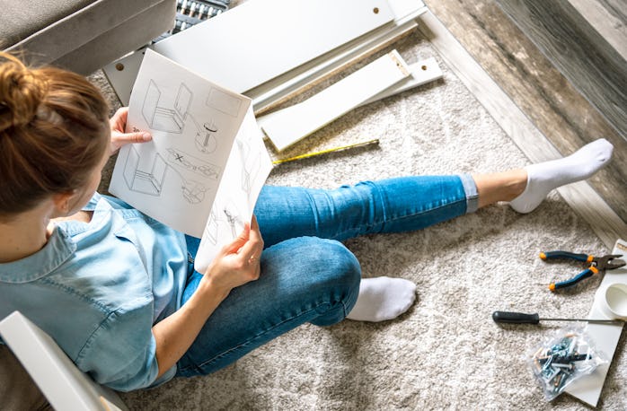 Concentrated young woman reading the instructions to assemble furniture at home in the living room