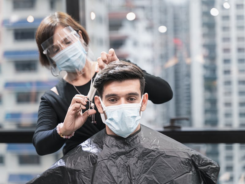 Hairdresser with security measures for Covid-19 or coronavirus, hair cut a man in a medicine mask, s...