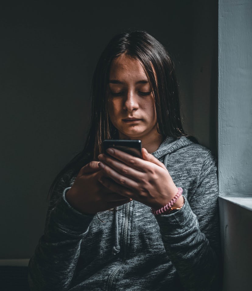 Teenage girl using smart phone in the dark. Sad teenager with mobile phone, scared of threatening, m...