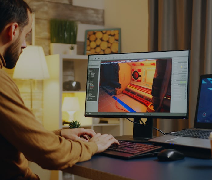 Male game developer typing on keyboard while developing a new level of the game.