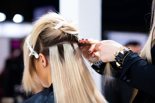 Professional hairdresser making hair extensions for blonde girl in a beauty salon