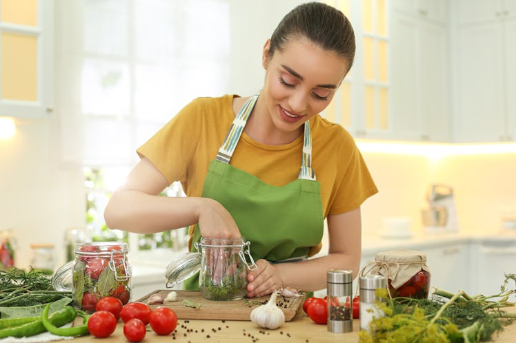 A woman puts dill into a jar for pickled garlic. 