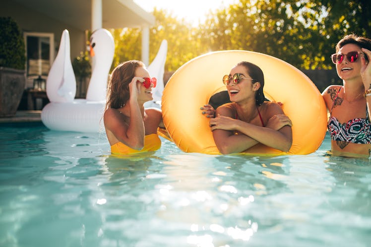 Happy young female friends in swimming pool with inflatable ring. Smiling women enjoying in a pool.