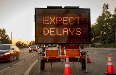 Mobile Electronic Traffic Sign stating “expect Delays” taken at sunset with traffic blurred driving ...