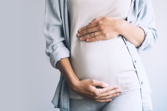 Pregnant woman holds hands on belly on white background. Mother waiting for baby birth. Women prepar...