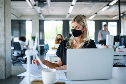 Young woman with face mask back at work in office after lockdown, working.
