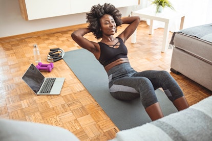 African american sportswoman doing abs on yoga mat near laptop in living room. African-American woma...