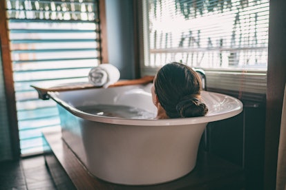 Bath taking woman relaxing in bathtub of hotel room at luxury overwater bungalow resort in Bora Bora...