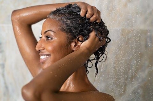 Woman washing hair showering in bathroom at home. Smiling black woman bathing while looking away. Ha...