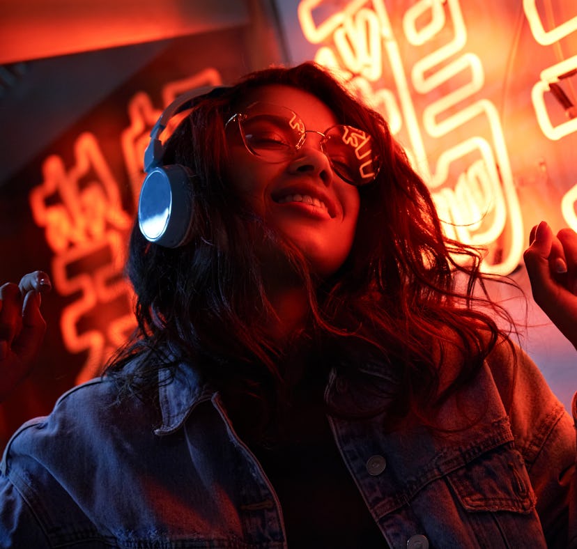 Woman dancing and listening to her headphones under neon lights. Sagittarius zodiac weaknesses inclu...