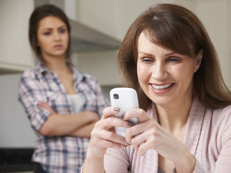 Mother Texts On Mobile Phone As Daughter Watches In Background