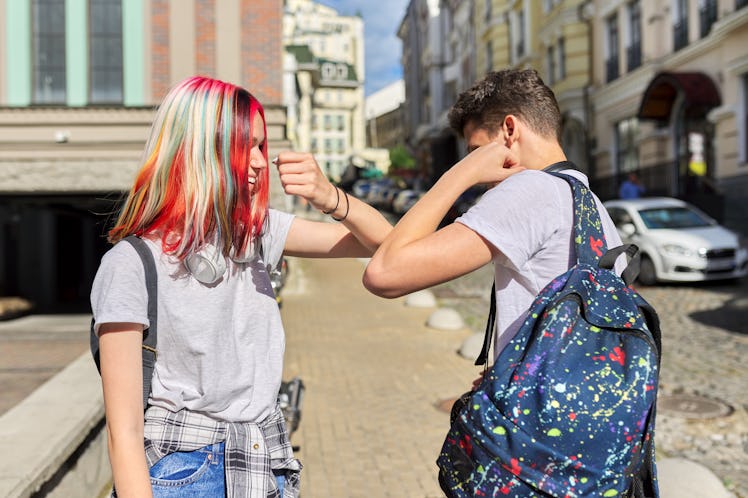 Two teenage friends greet each other by bumping elbows, maintaining distance during pandemic reopeni...