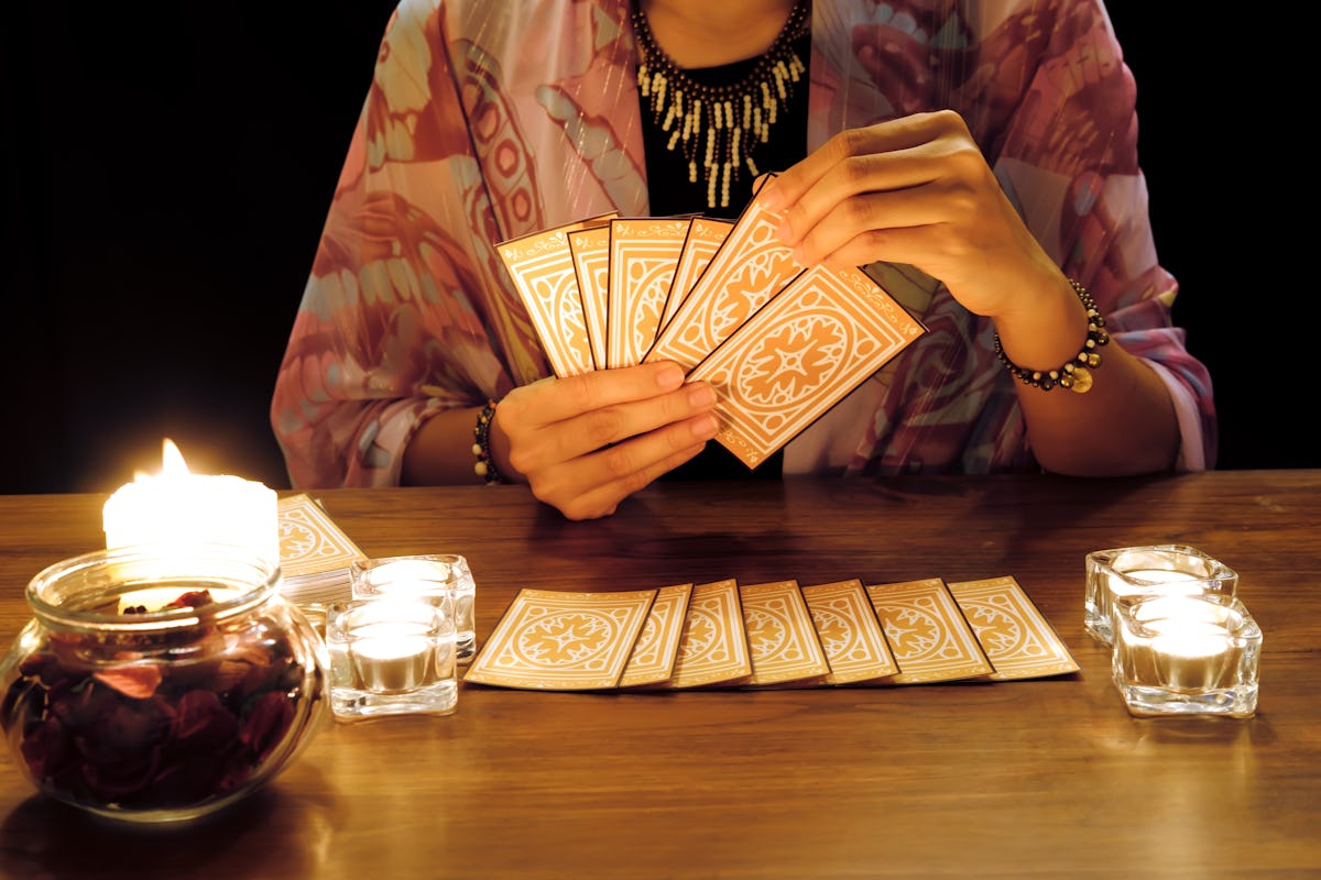 Tarot reading or fortune teller holding and picking tarot cards in her hands with burning candles and tarot cards spreading on a wooden table.Divination or forecasting concept.