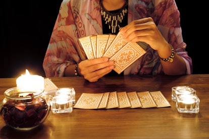 Tarot reading or fortune teller holding and picking tarot cards in her hands with burning candles an...