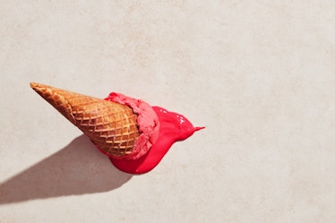 Strawberry ice cream with waffle cone dropped on the floor and melting on the ground under hot summe...